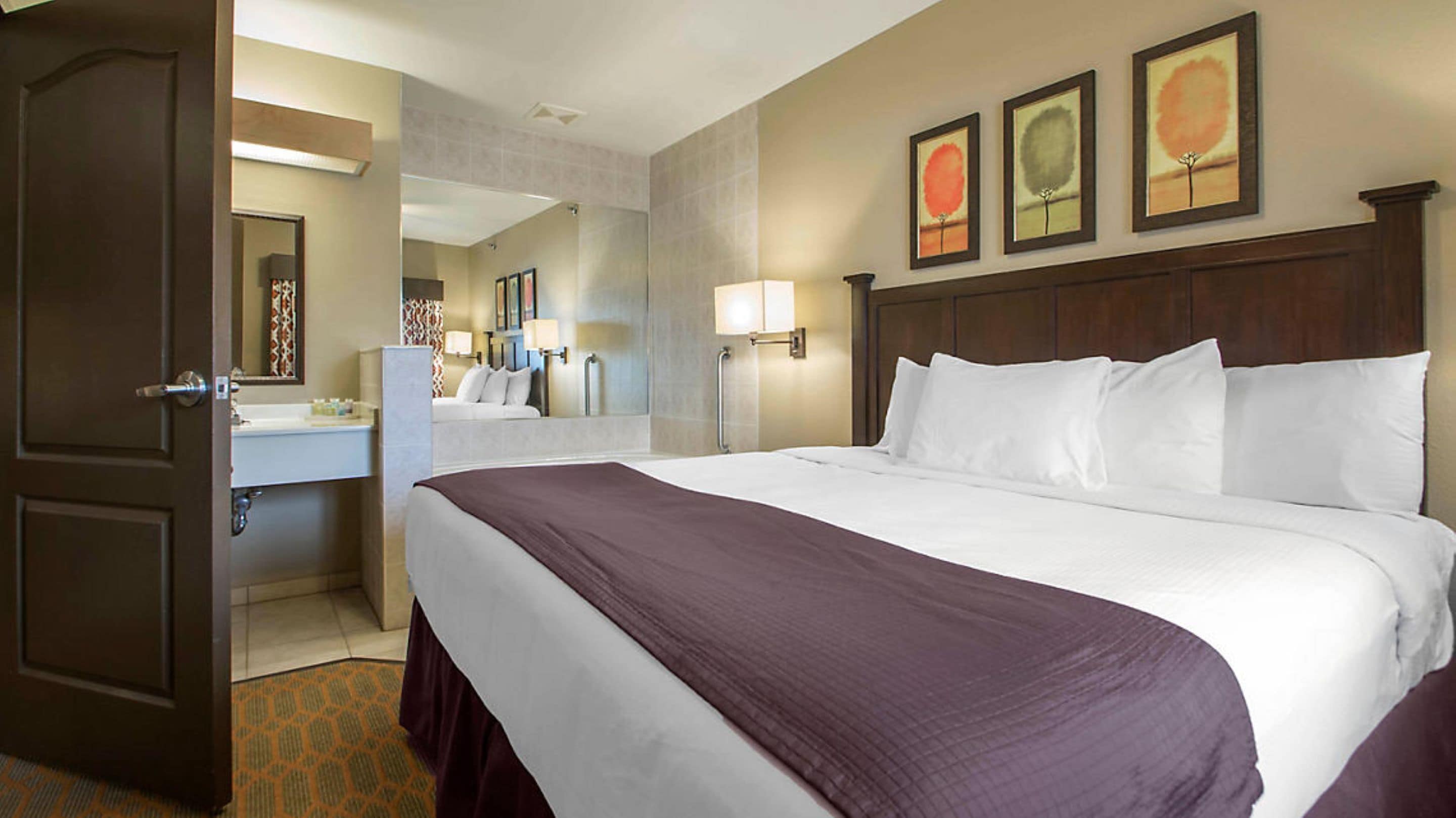 A hotel room with a large bed, a bedside table, a mirror, and three framed pictures on the wall.