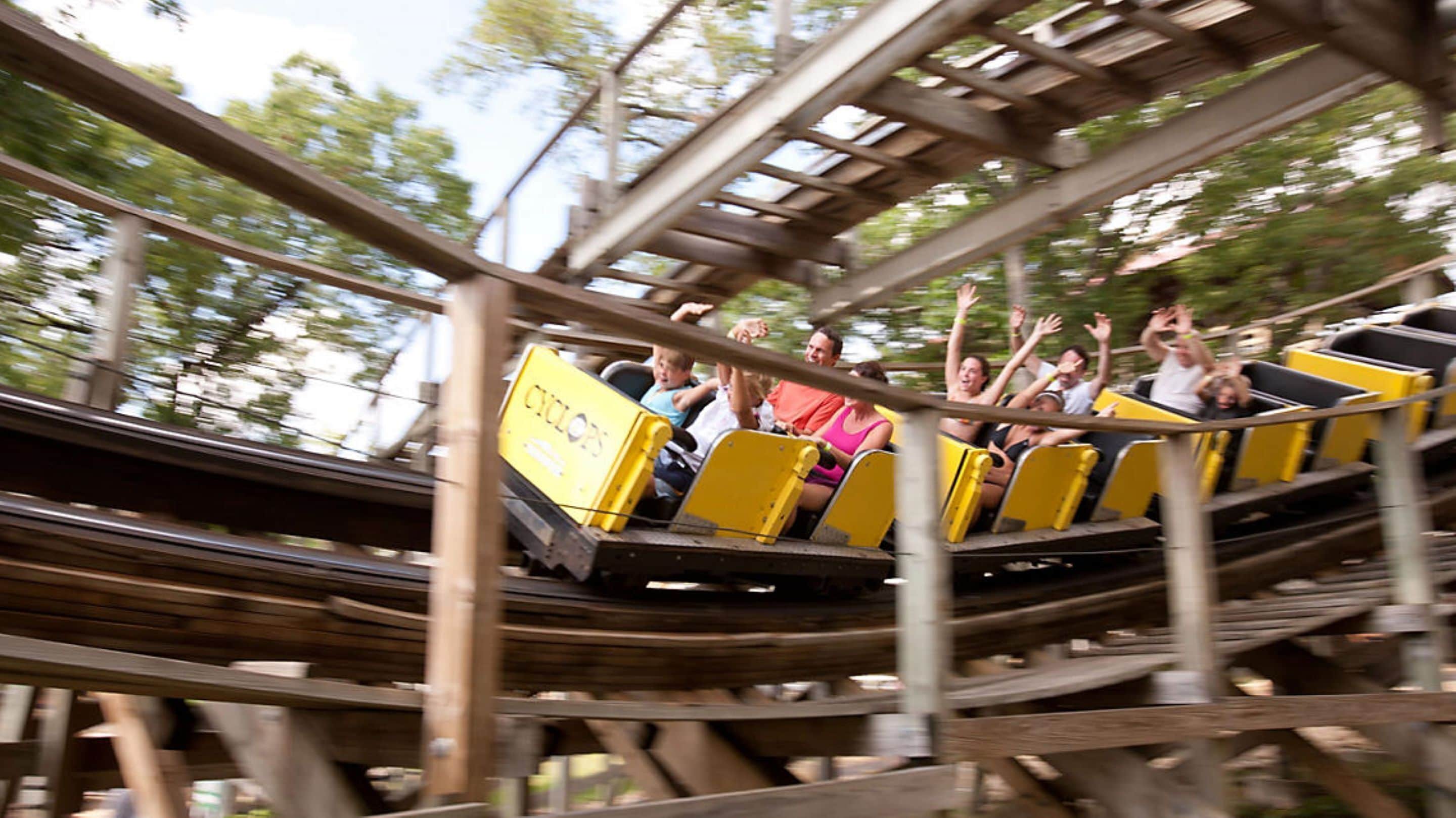 A wooden roller coaster with yellow cars and passengers.