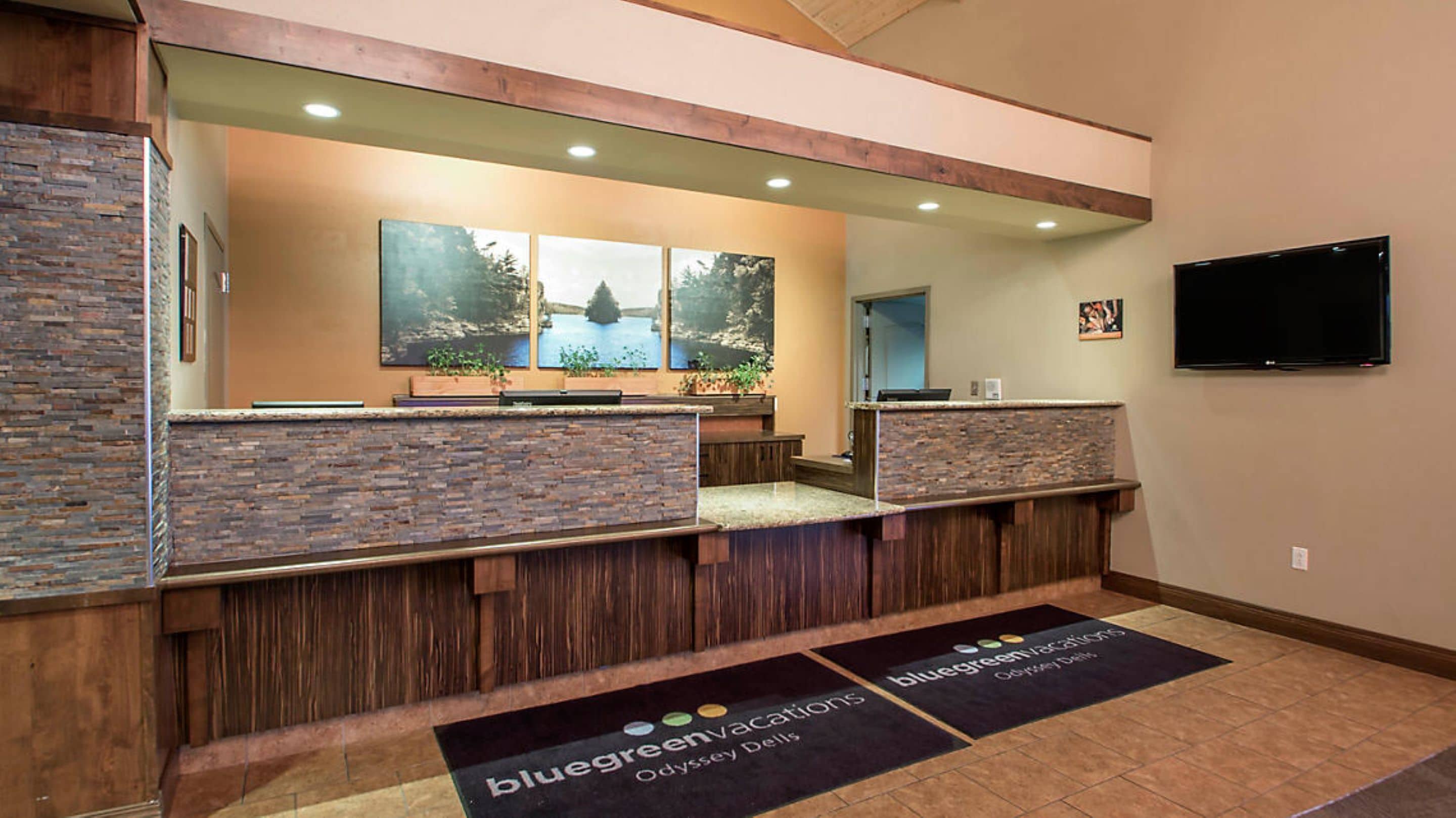 A reception area with a stone and wood reception desk, a large mirror, and a flat-screen TV mounted on the wall.