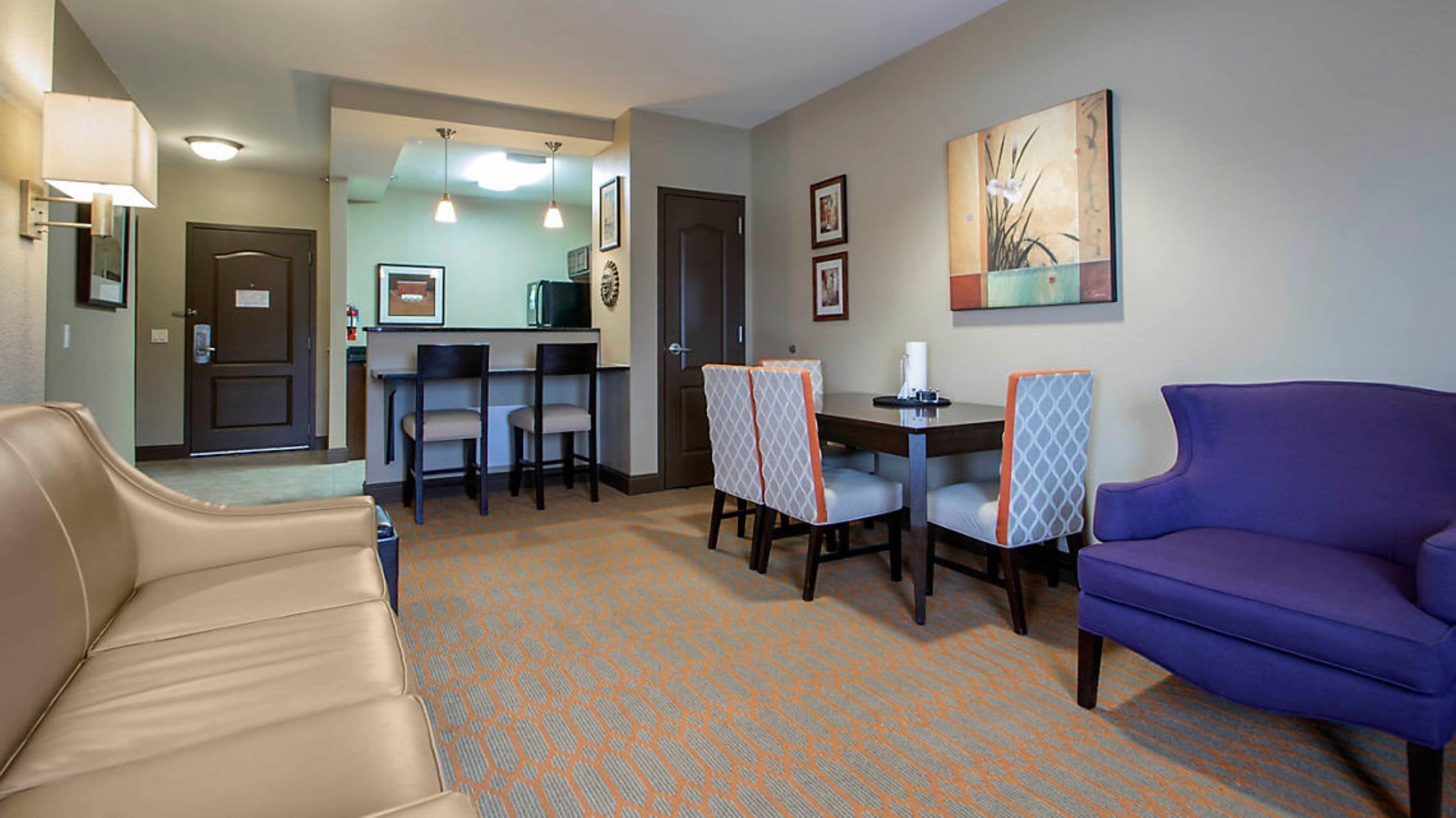 A hotel room with a sofa, a dining table with chairs, a kitchen area, and a living area with a couch.