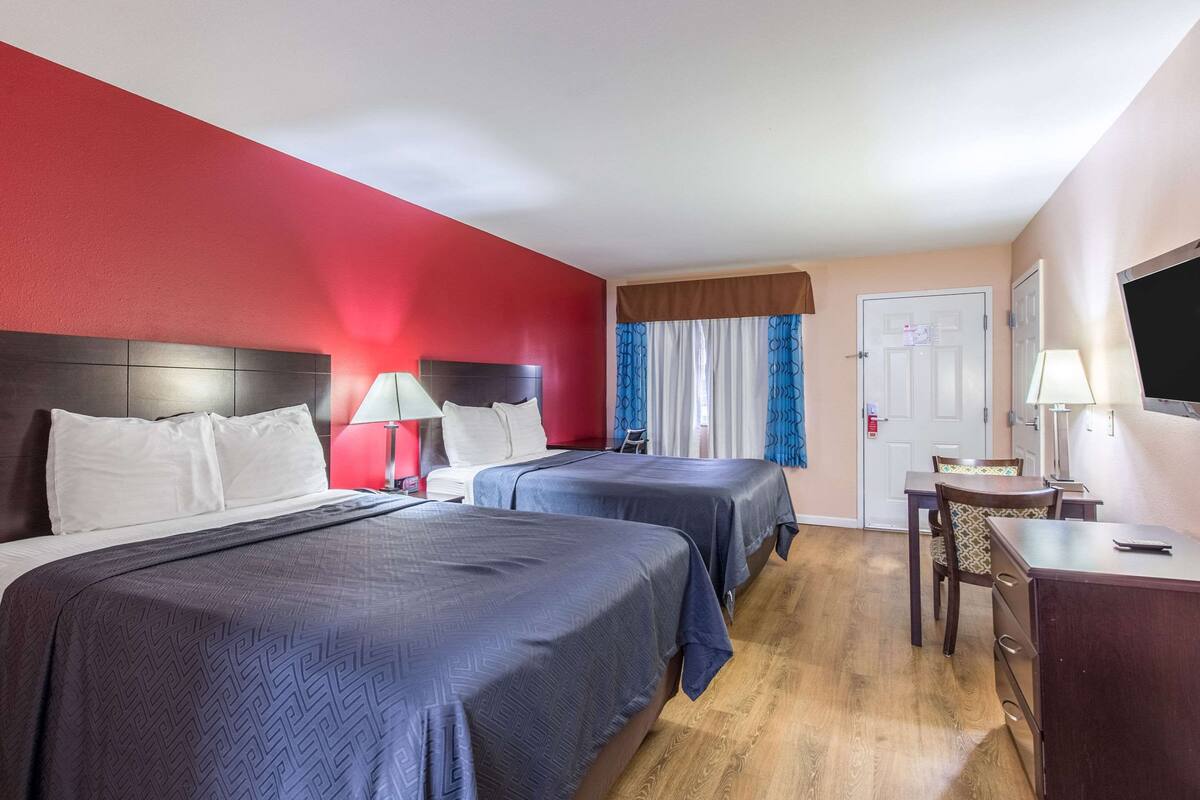 A hotel room with two beds, a desk, a chair, and a TV.