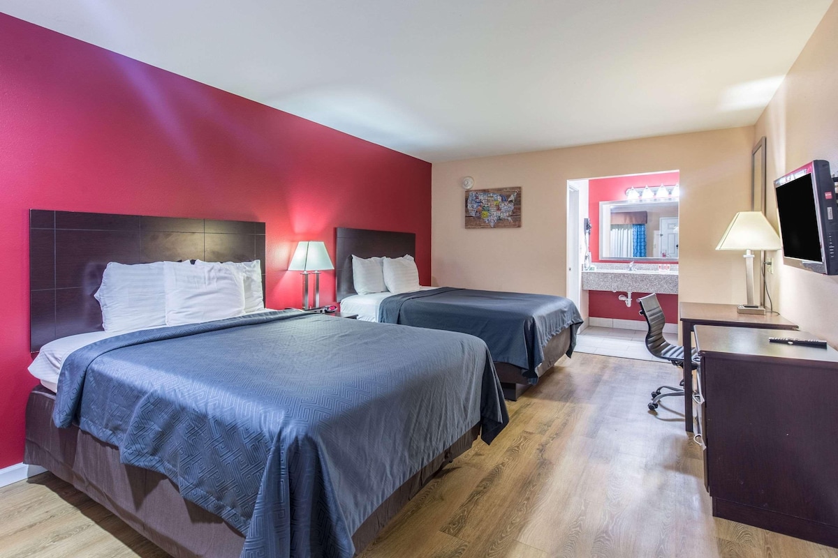 A hotel room with two beds, a desk, a chair, and a TV.