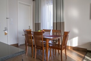Un comedor con una mesa y sillas de madera, un frutero y vistas al exterior a través de cortinas translúcidas.