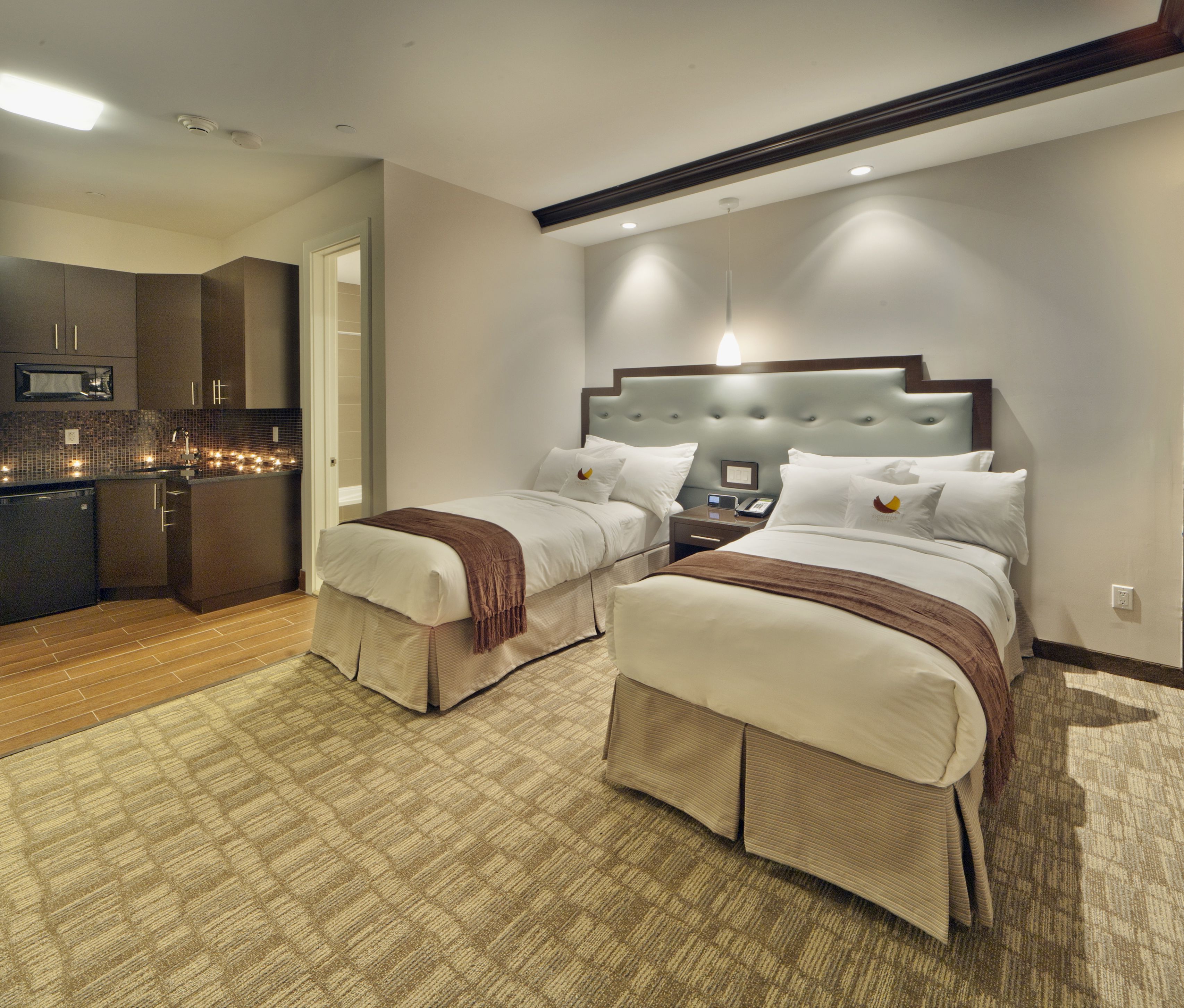 A hotel room with two beds, a kitchenette, and a bathroom.