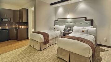 A hotel room with two beds, a kitchenette, and a bathroom.