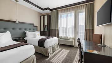 A hotel room with two beds, a desk, a TV, and a large window with curtains.