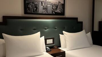 Een hotelkamer met twee bedden, een stadsgezichtschilderij boven het hoofdeinde, een nachtkastje met een telefoon en een spiegel aan de muur.