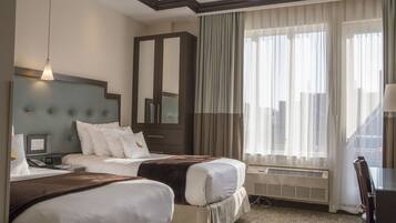 A hotel room with two beds, a large mirror, a desk, and a view of the city through large windows.