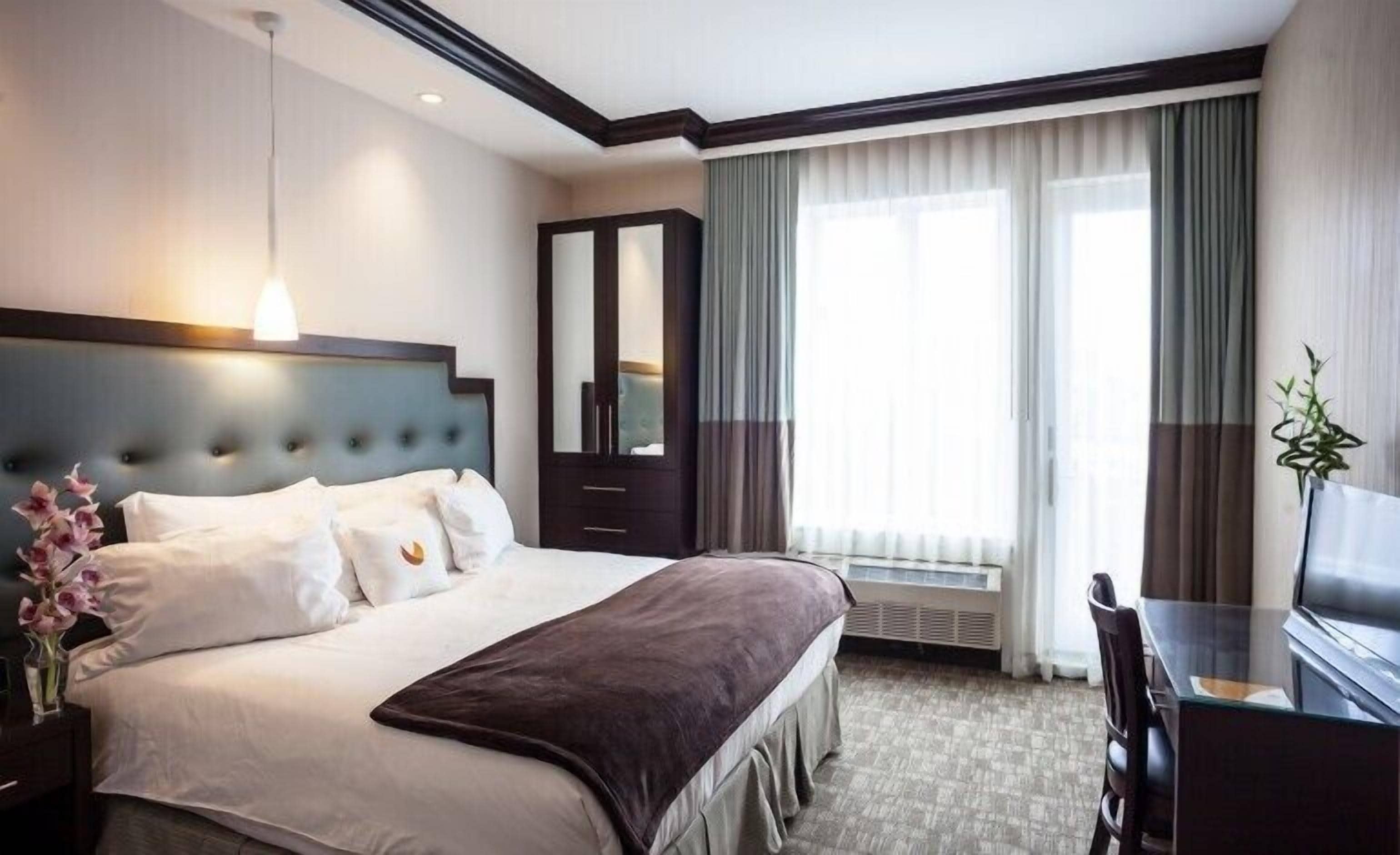 Quarto de hotel com uma cama grande, cômoda, escrivaninha e uma janela com cortinas.