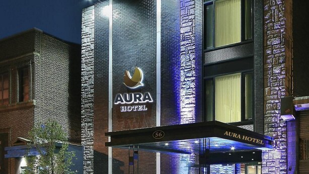 Egy modern hotel, amelyen feltűnő tábla hirdeti az „AURA HOTEL” nevet, és egy nagy „56”-os szám jelzi a címét.