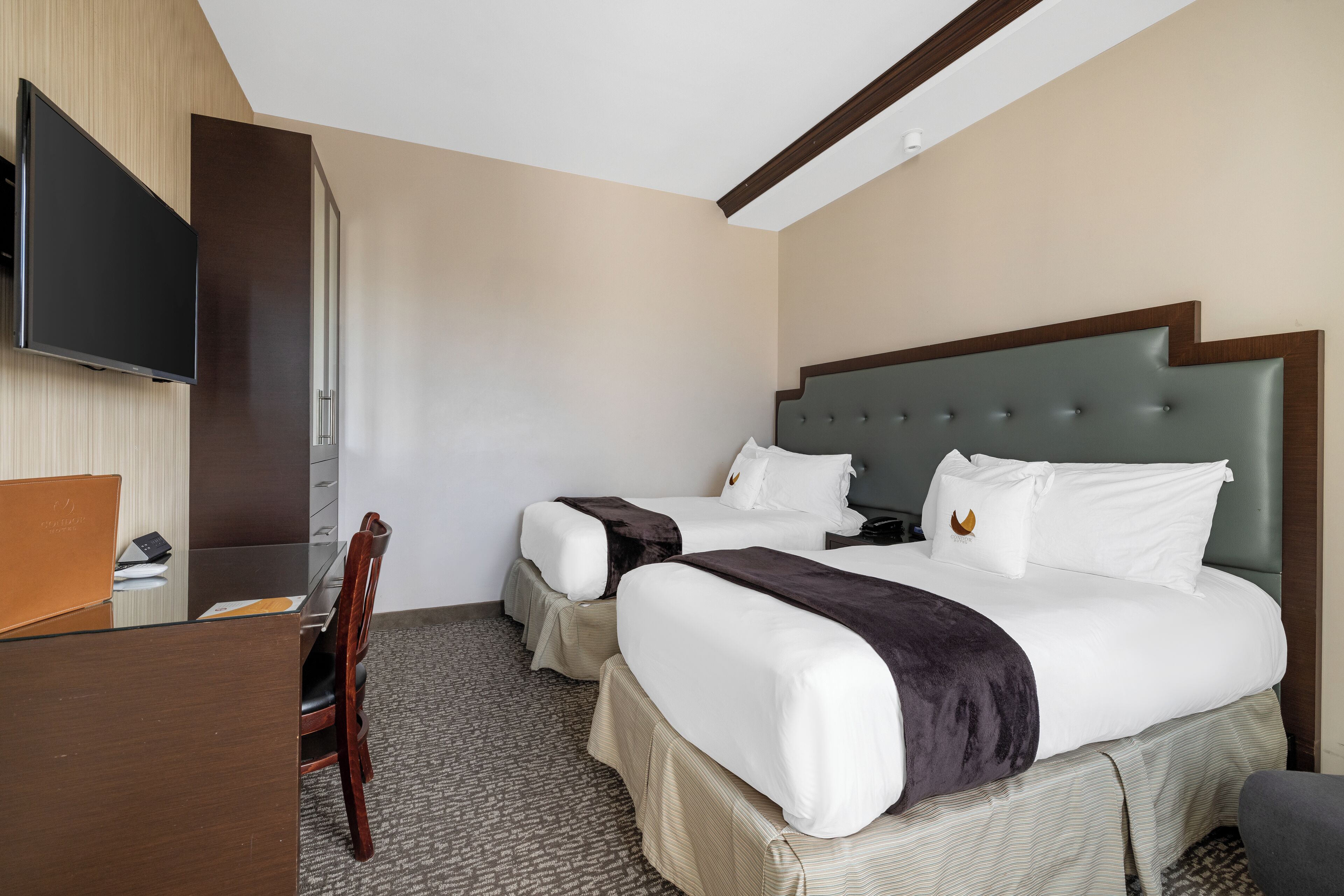 A hotel room with two beds, a desk, and a television.