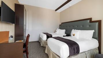 A hotel room with two beds, a desk, and a television.