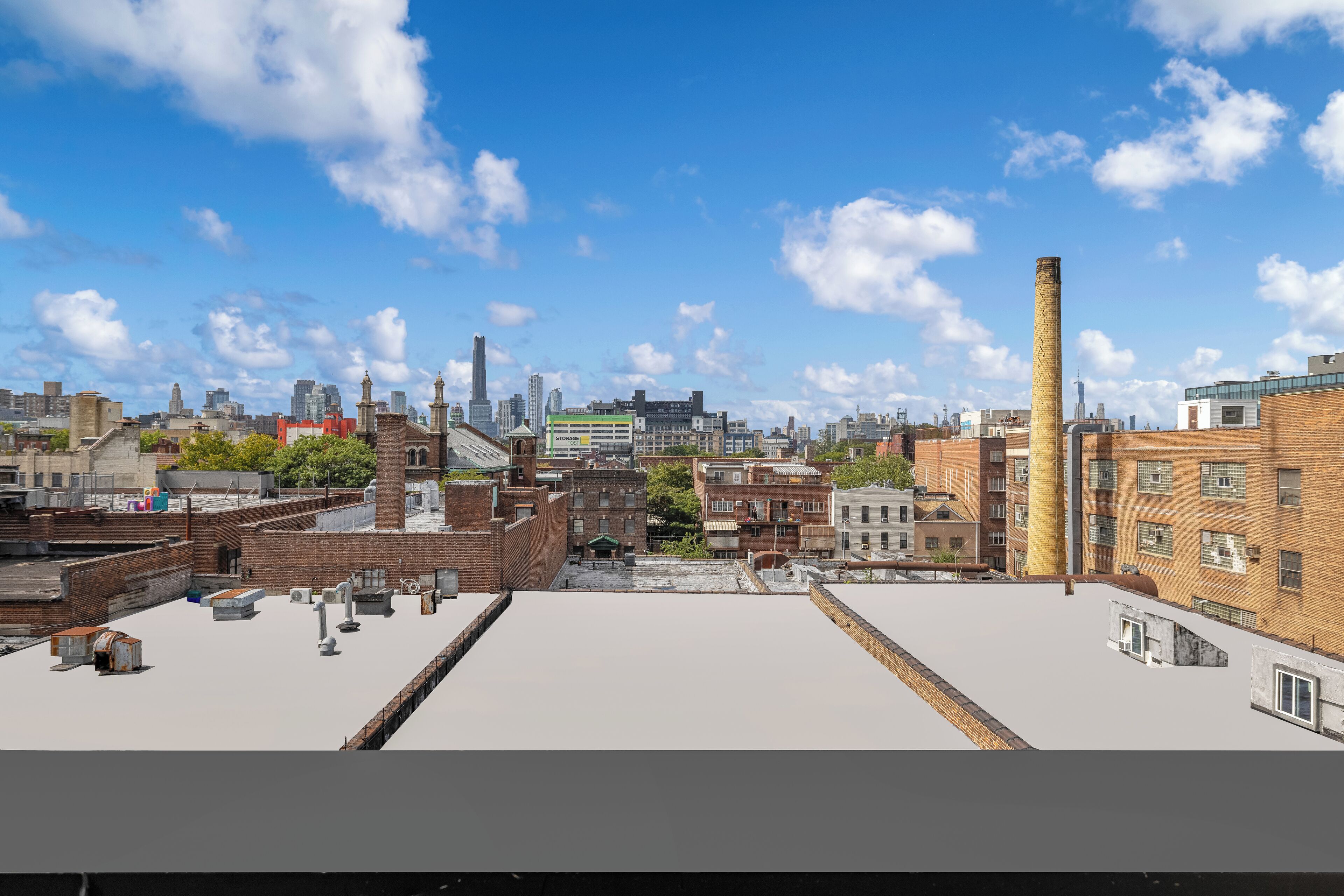 Une terrasse offrant une vue dégagée sur les toits d’une ville, avec différents bâtiments et une cheminée imposante.