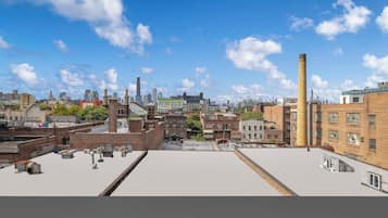 Une terrasse offrant une vue dégagée sur les toits d’une ville, avec différents bâtiments et une cheminée imposante.