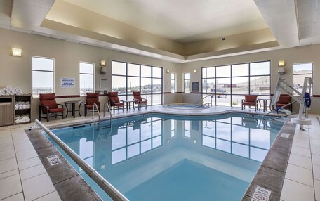 A pool area with a clear view of the sky through large windows, a pool with a safety ladder, and several lounge chairs.