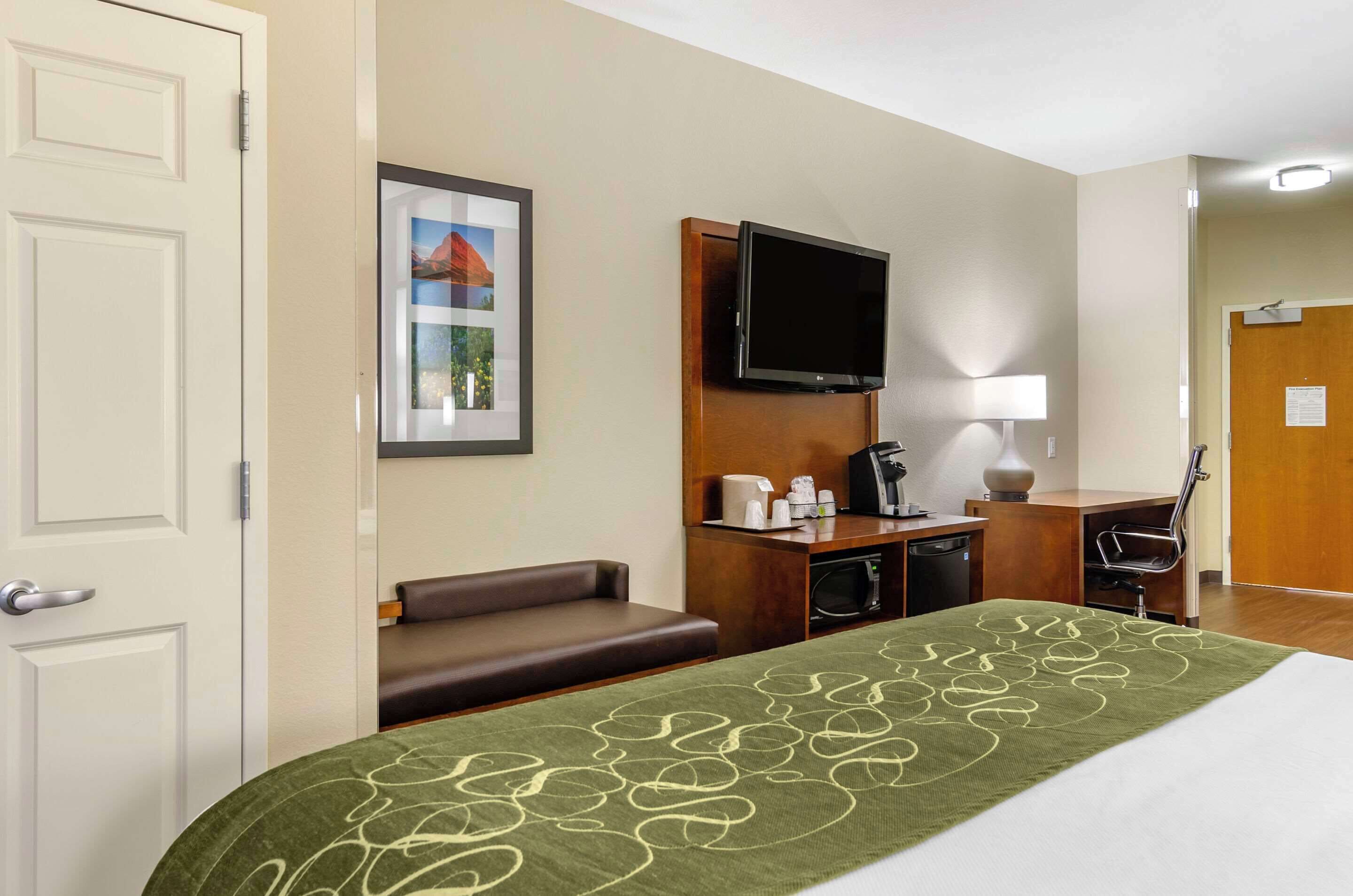 A hotel room with a bed, a desk, a television, a couch, and a door.