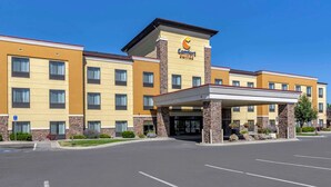 Ein Comfort Suites Hotel mit modernem Design, ausgestattet mit einem zentralen Eingangsbereich und einem überdachten Gang, mehreren Stockwerken und einem strahlend blauen Himmel.