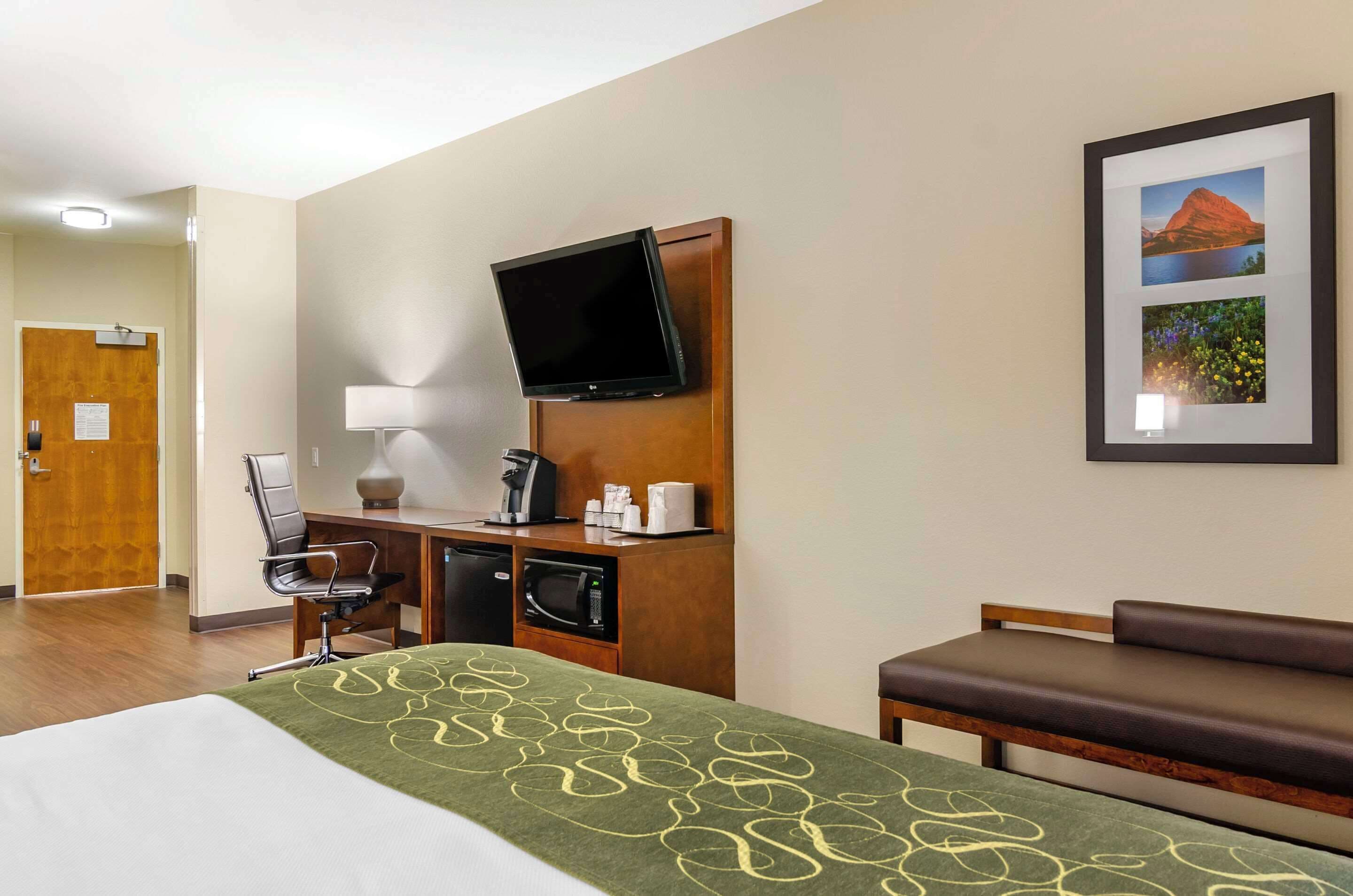 A hotel room with a bed, a desk with a computer, a TV, a coffee maker, and a framed picture on the wall.