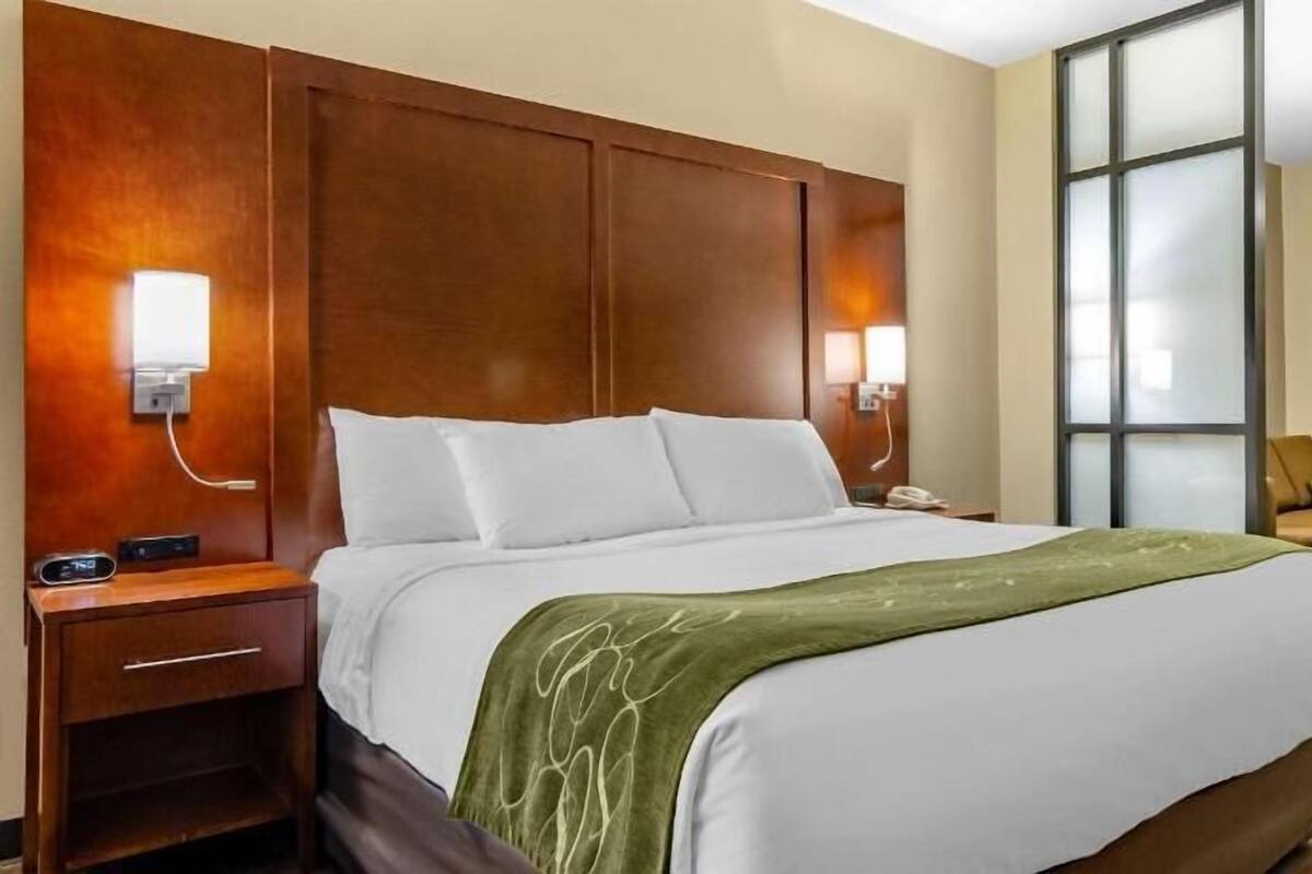 Ein Hotelzimmer mit einem großen Bett, Nachttischen, einem Schreibtisch, einem Sessel und einem großen Fenster.
