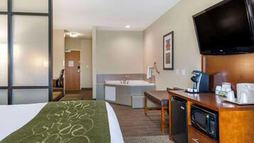 A hotel room with a bed, a desk with a microwave, a coffee maker, and a TV.