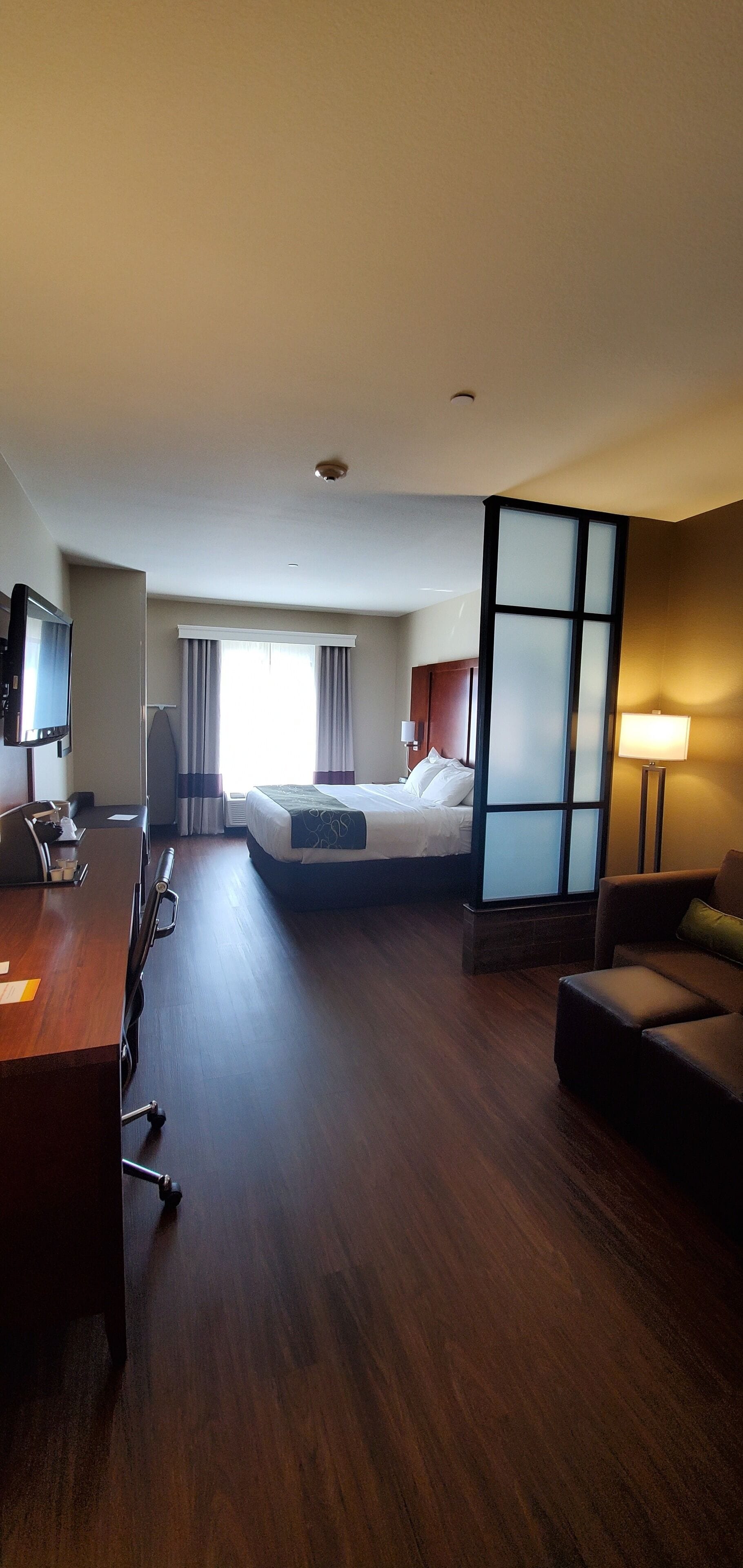 A hotel room with a bed, a desk, a chair, a TV, and a lamp.
