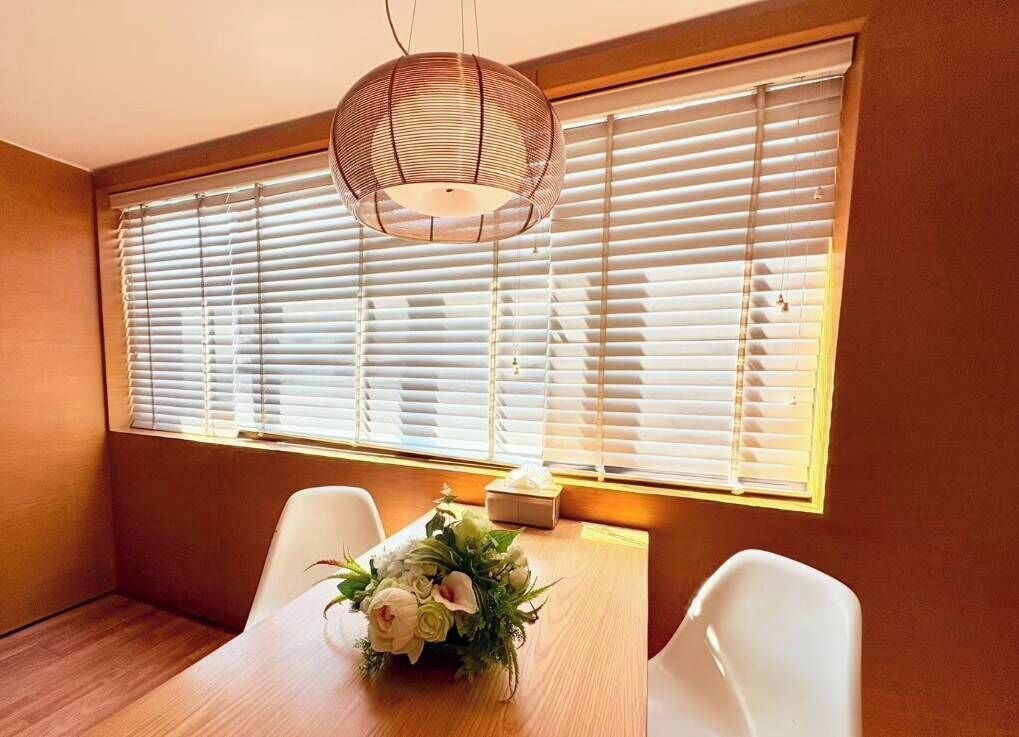 A dining area with a wooden table, white chairs, a floral centerpiece, and a woven pendant light.
