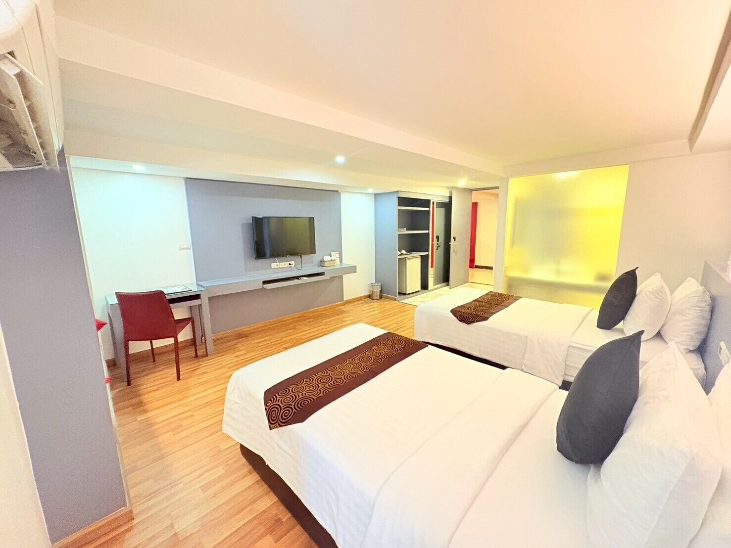 A hotel room with two beds, a desk with a chair, a television, and a wardrobe.