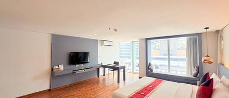 Habitación de hotel con una cama grande, televisión montada en una pared gris, escritorio y ventana con vista a la ciudad.