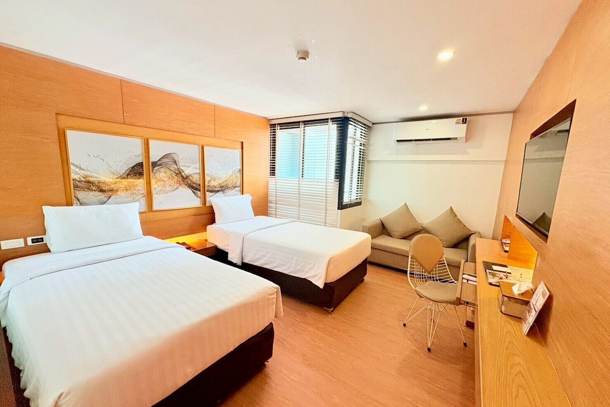 A hotel room with two beds, a sofa, a desk, and a TV.