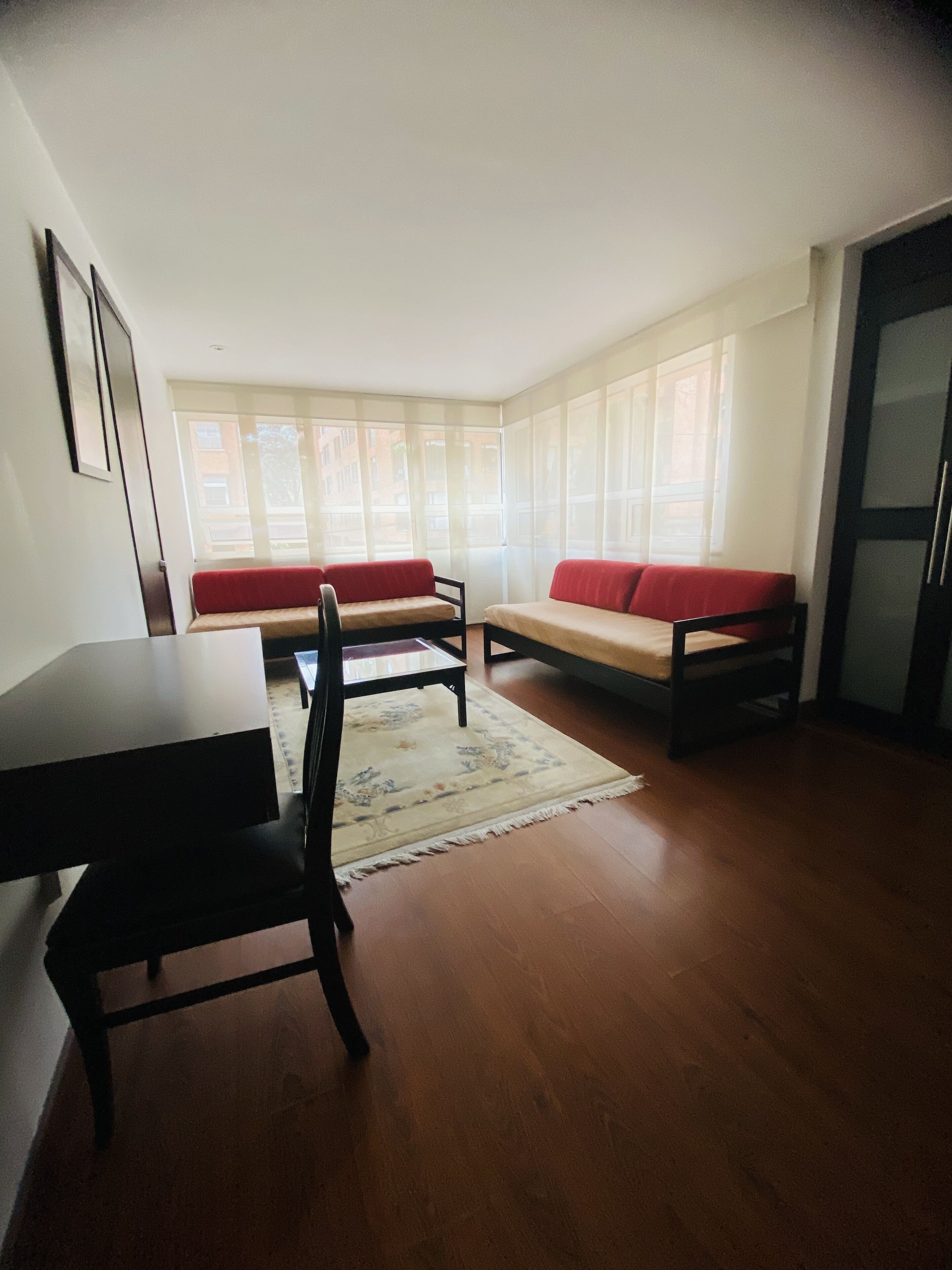 A room with a dining table, two chairs, a sofa, and a rug.