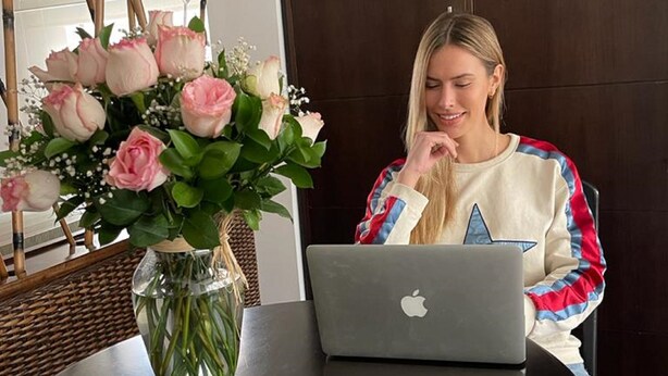 A person sitting at a round table with a laptop, a vase of flowers, and a wooden chair. - Hotel Retiro 84 (Bogotá)