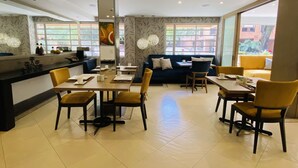A modern dining area with a central seating arrangement, a kitchen counter, and large windows providing natural light. - Hotel Retiro 84 (Bogotá)