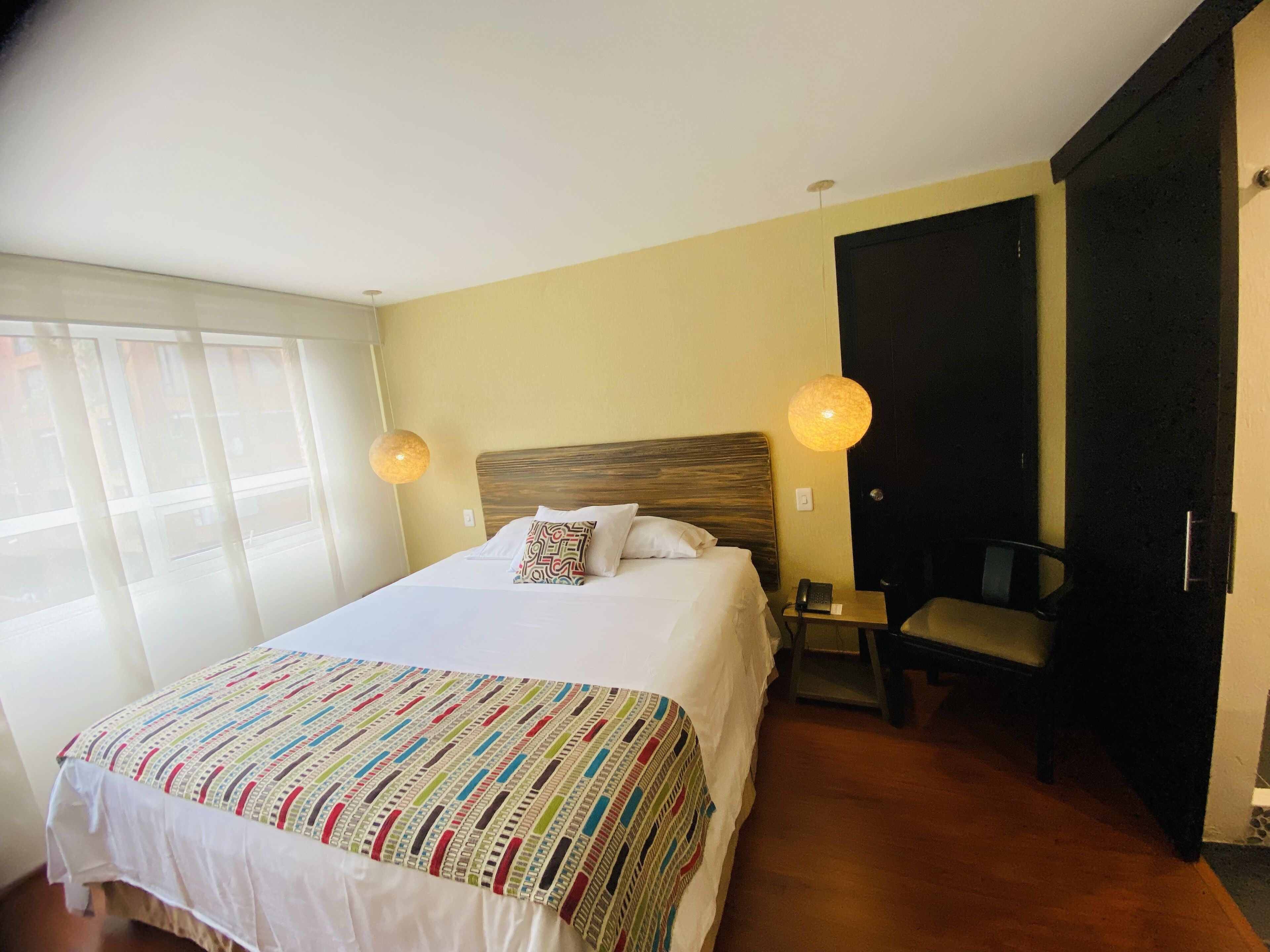 A hotel room with a large bed, two bedside lamps, a chair, and a door.