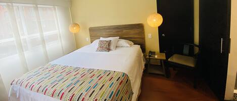 A hotel room with a large bed, two bedside lamps, a chair, and a door.