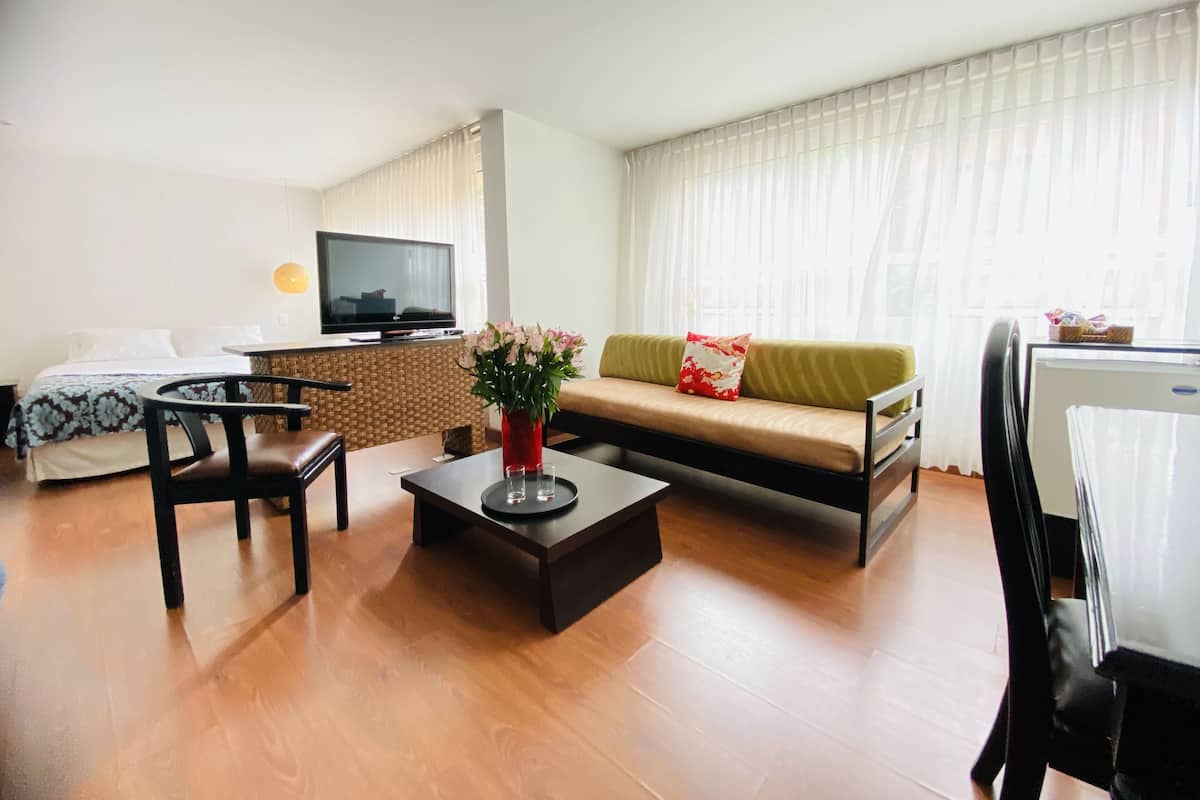Una sala de estar bien iluminada con un sofá, una mesa de centro, un televisor y una cama.