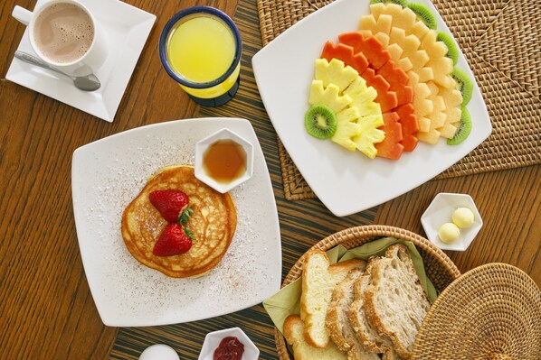 A breakfast setting with pancakes, fruit, toast, and beverages on a wooden table. - Hotel Retiro 84 (Bogotá)