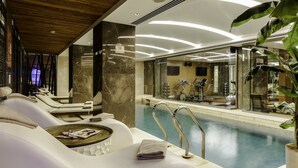 A luxurious indoor pool area with a spa, exercise equipment, and a seating area with a tray of magazines. - Levni Hotel & Spa - Special Class (Istanbul)