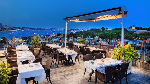 An outdoor dining area with tables and chairs, overlooking a body of water and a cityscape. - Levni Hotel & Spa - Special Class (Istanbul)