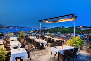 An outdoor dining area with tables and chairs, overlooking a body of water and a cityscape. - Levni Hotel & Spa - Special Class (Istanbul)