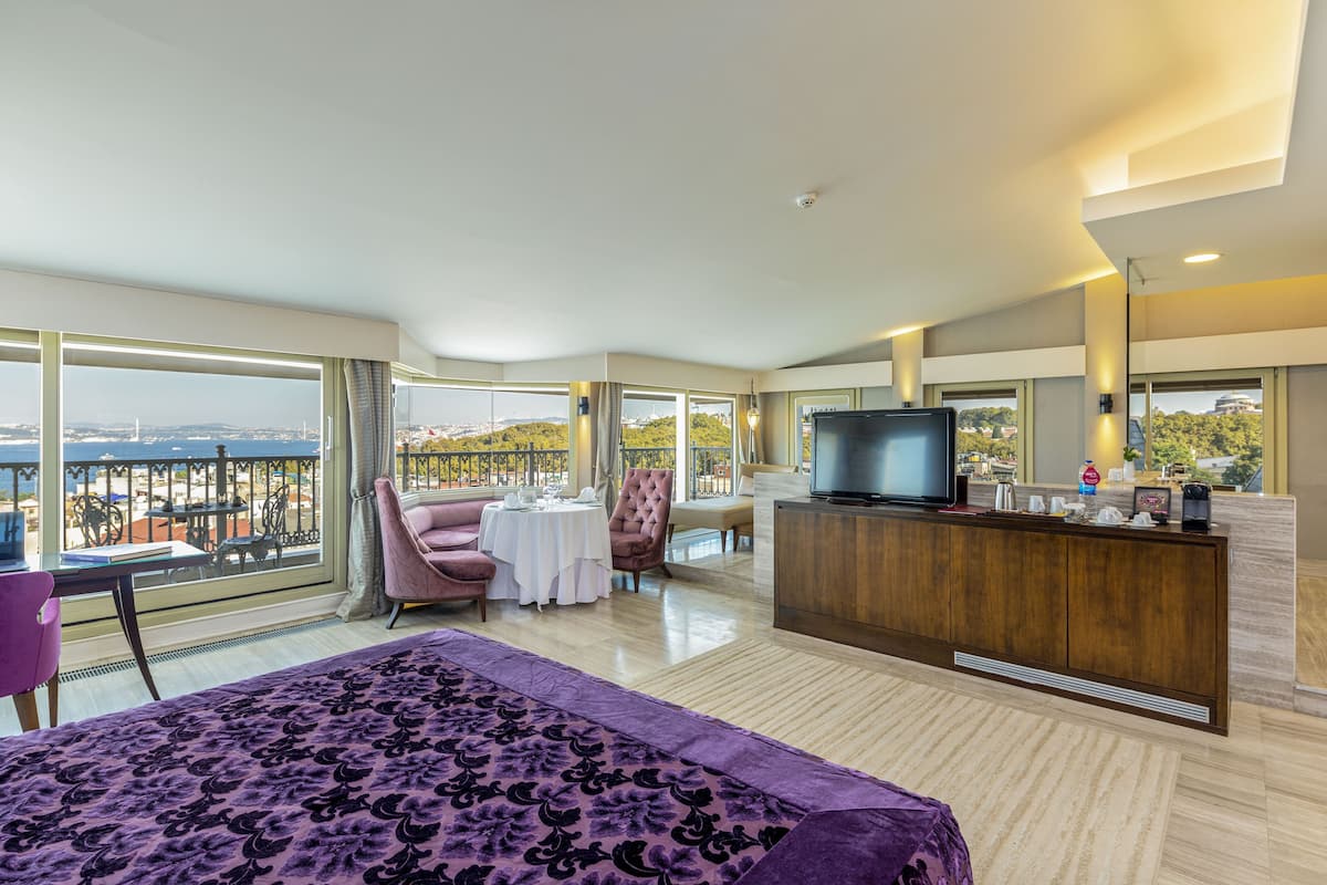 Une chambre d’hôtel spacieuse, dotée d’un grand lit, d’une télévision, d’un coin repas et d’un balcon offrant une vue sur la ville.