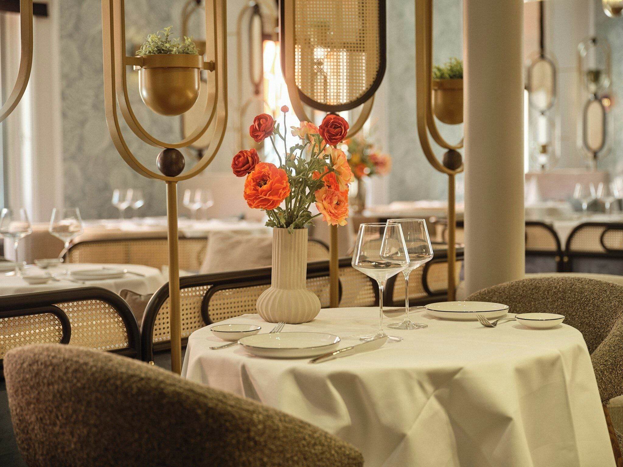 Una mesa de comedor dispuesta con platos, cubiertos y copas de vino, con un jarrón de flores en el centro.