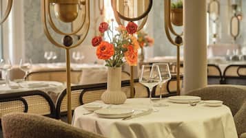 Una mesa de comedor dispuesta con platos, cubiertos y copas de vino, con un jarrón de flores en el centro.