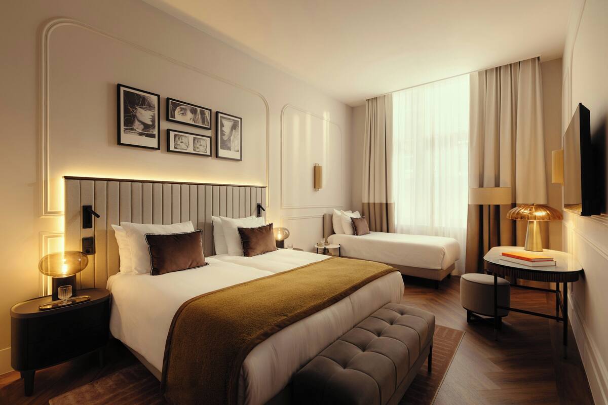 A hotel room with a large bed, a smaller bed, a seating area, a TV, and framed pictures on the wall.