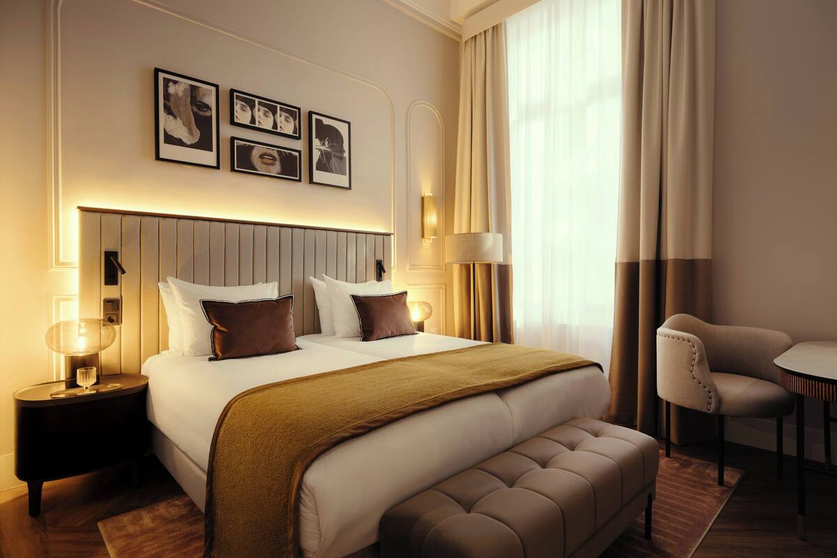 A hotel room with a large bed, a bedside table with a lamp, a chair, and a small table.