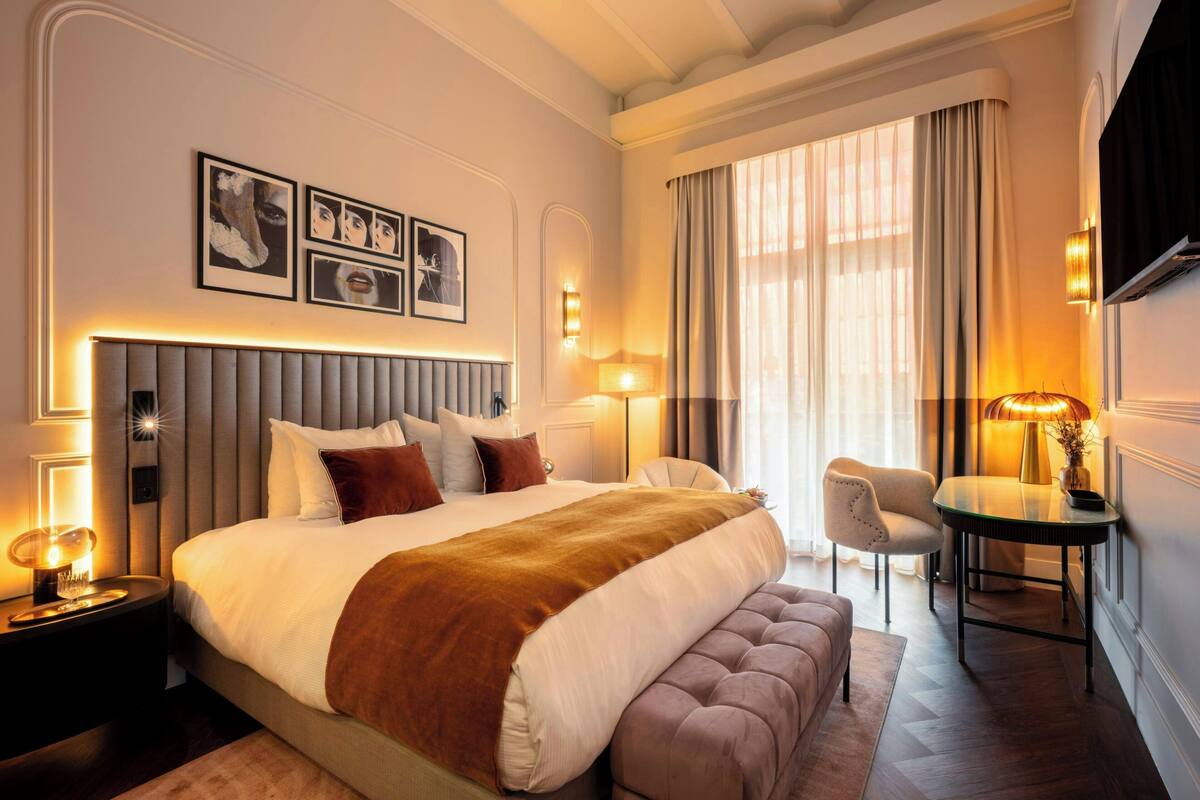 A hotel room with a large bed, bedside tables, a chair, a small table, and a TV.