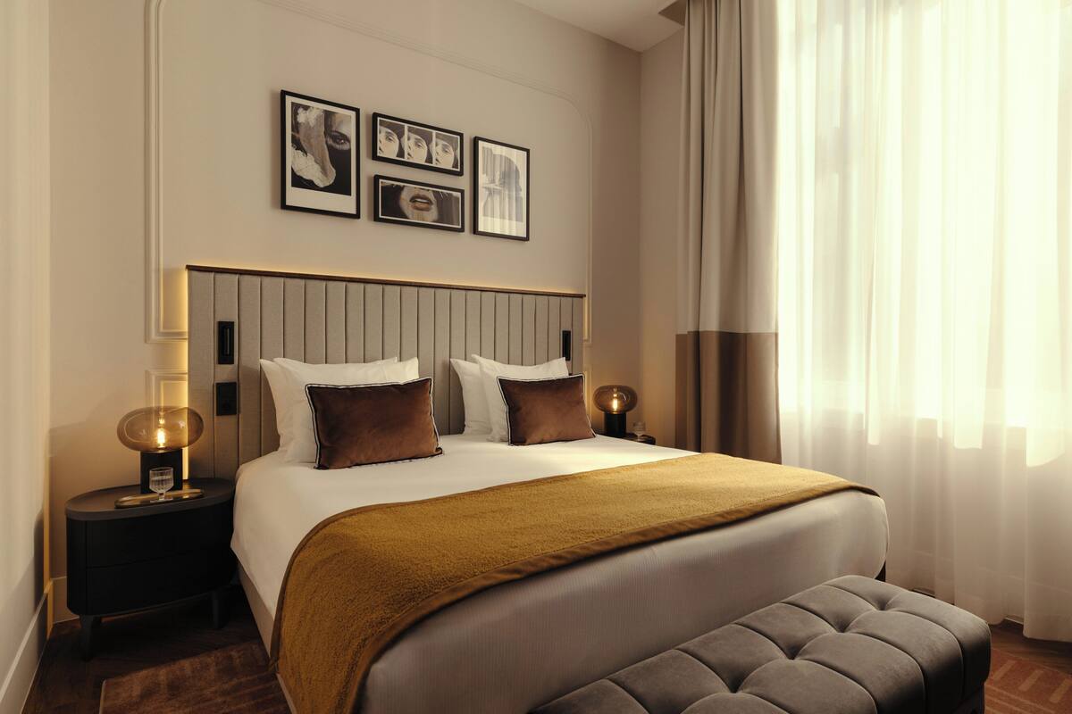 A hotel room with a large bed, bedside tables with lamps, a headboard, and framed pictures on the wall.
