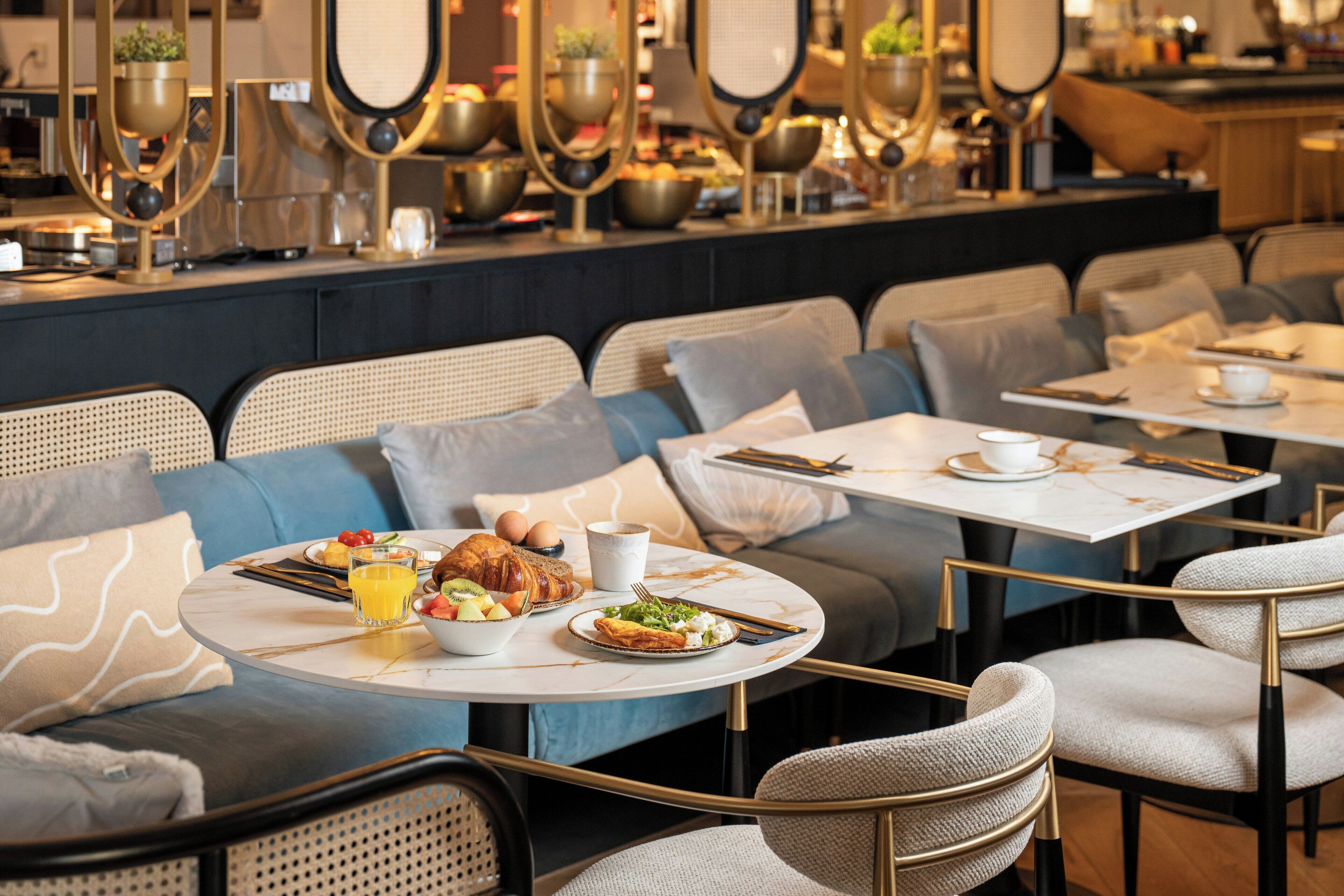 A restaurant with round tables, cushioned seating, and a bar area with decorative items.