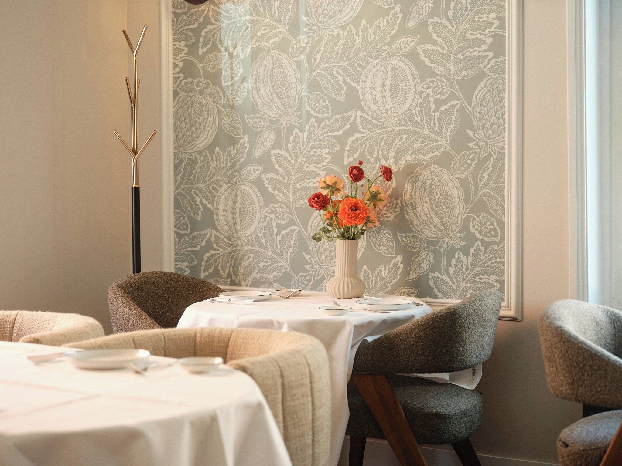 Un coin repas avec une table dressée pour deux personnes, un vase rempli de fleurs et un papier peint à motifs.