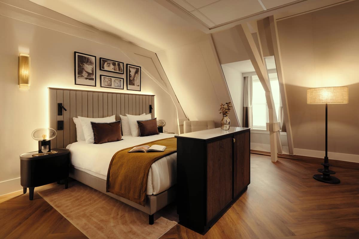 Un dormitorio con cama, mesitas de noche, un escritorio, una lámpara y cuadros en la pared.