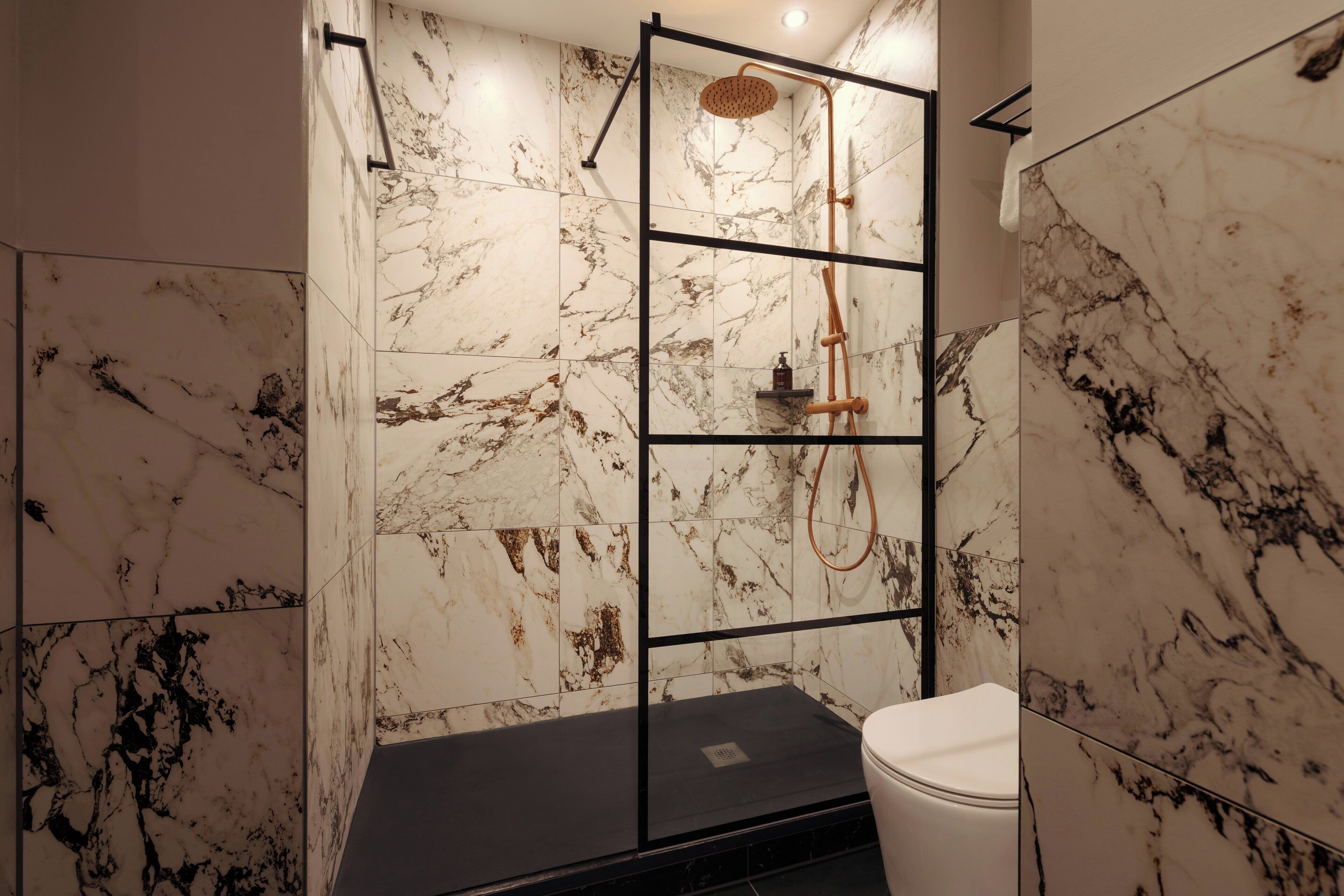 A bathroom with marble walls, a black floor, and a white toilet.